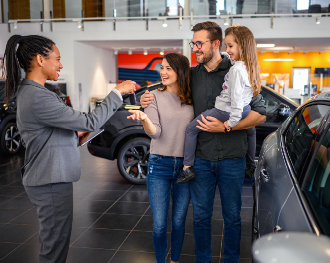 Image of family receiving keys to a car from car salesperson inside a dealership.