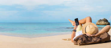 Image of a person lounging on a beach holding their phone.