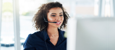 Image of a woman with a phone headset in front of a computer.